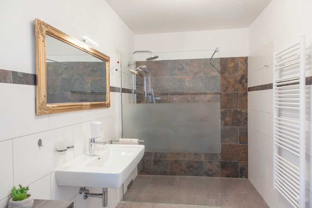 „Hahns Herberge“ – Innenaufnahme; Badezimmer mit Spiegel, Waschbecken und Dusche, Innenaufnahme; gepflegte Ausstattung und Details.